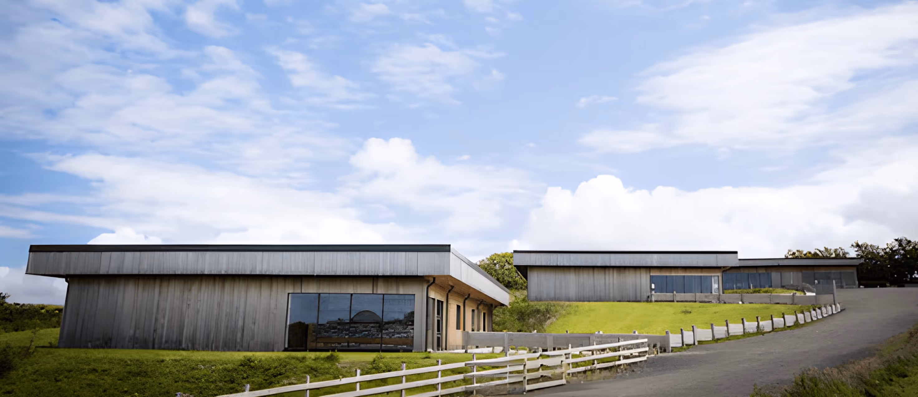 Modern buildings with large windows and metal paneling on a grassy hill under a partly cloudy sky.