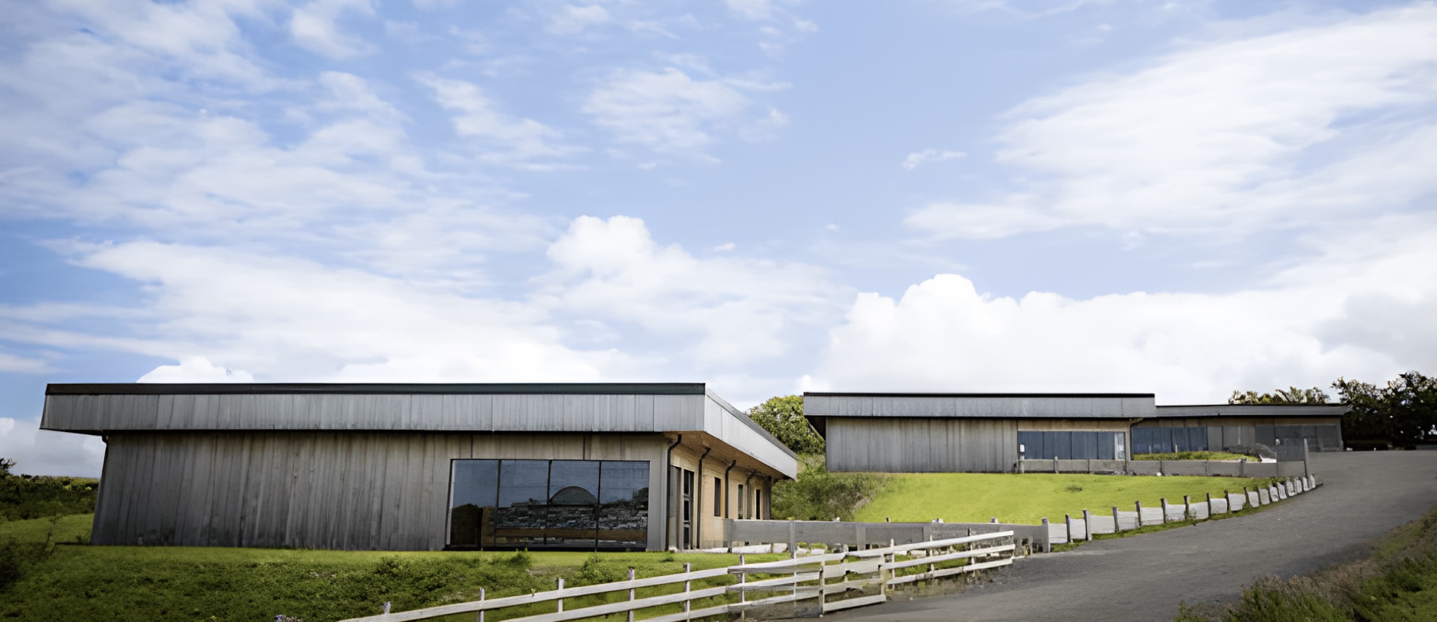 Modern buildings with large windows and metal paneling on a grassy hill under a partly cloudy sky.