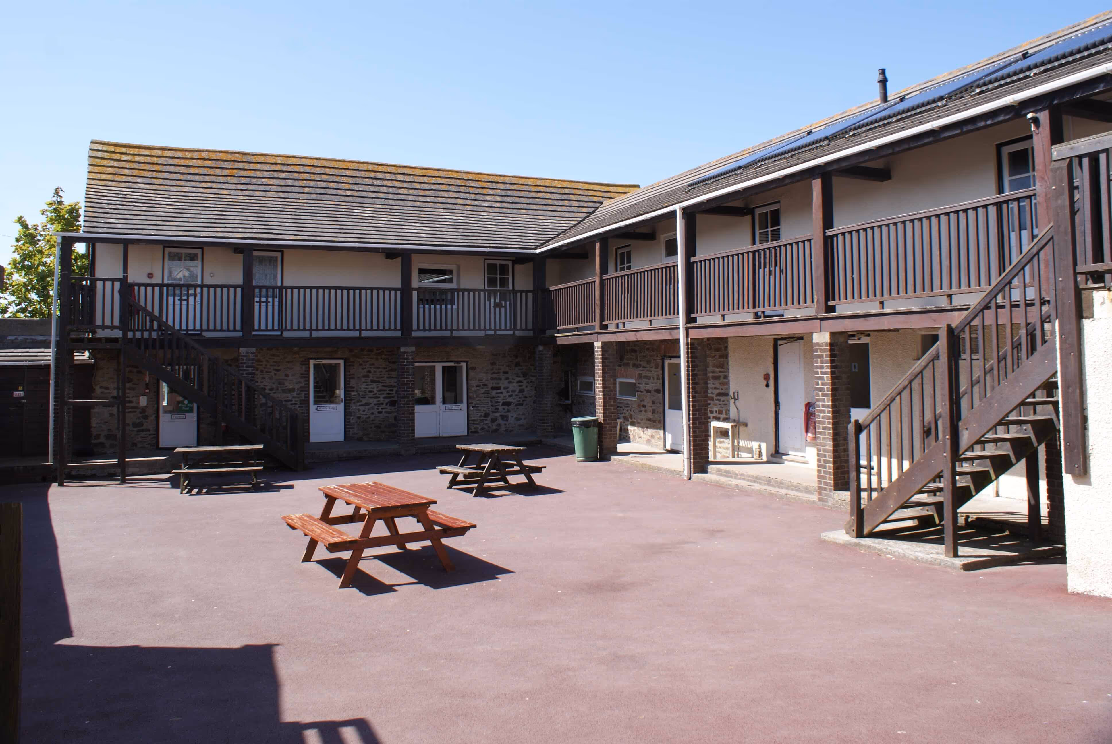 Courtyard with wooden picnic tables surrounded by two-storey stone and wood buildings with outdoor staircases.