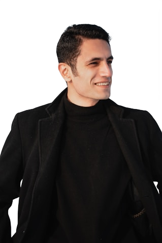 Smiling man with short dark hair wearing a black coat and turtleneck sweater, looking to the side.