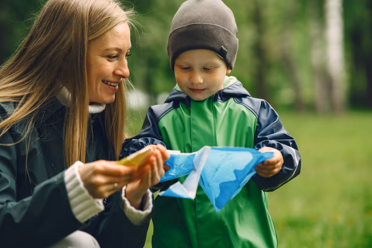 Smiling woman and young boy holding a blue kite outdoors in a green park.