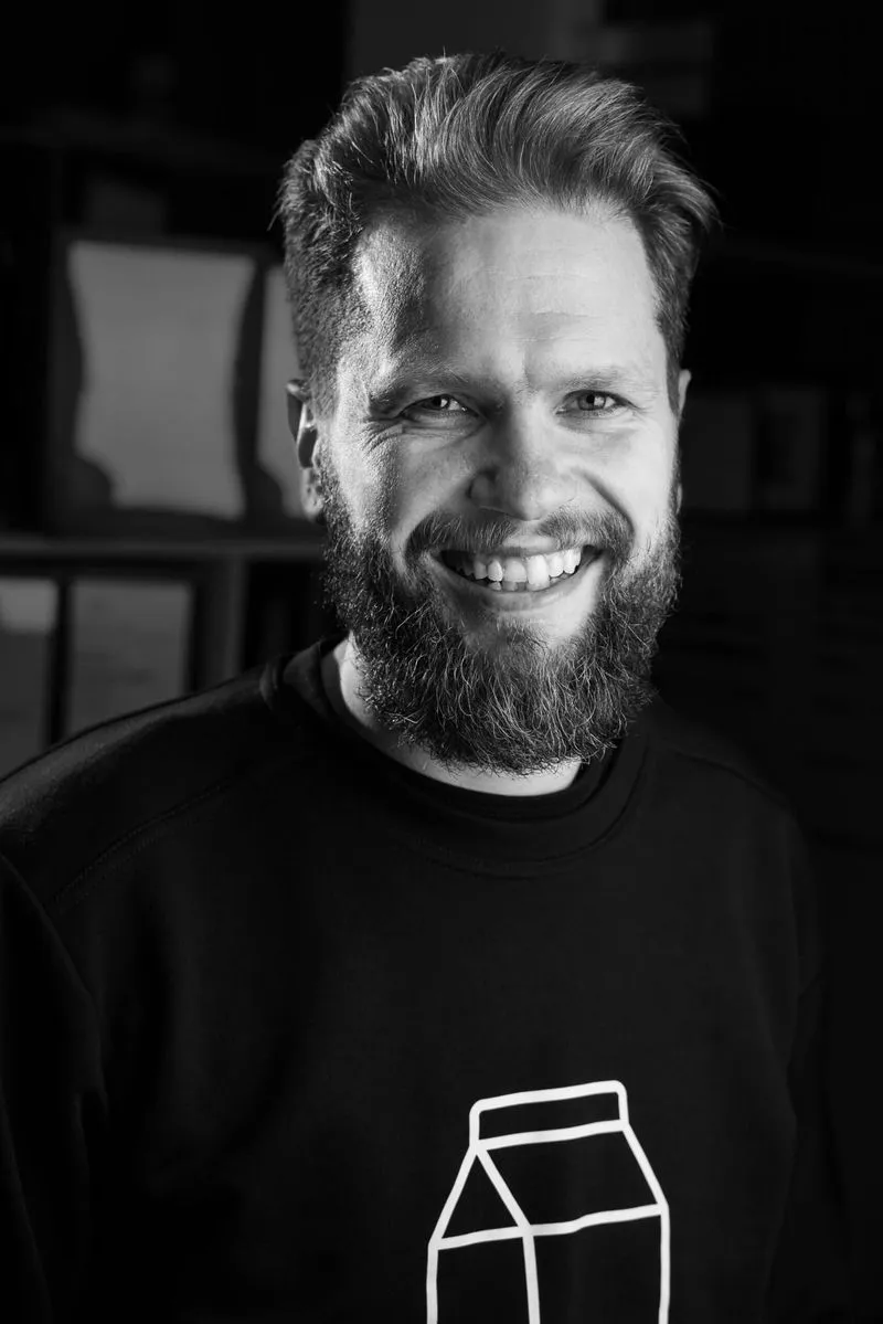 Smiling man with a beard and styled hair wearing a black sweatshirt with a white carton design.
