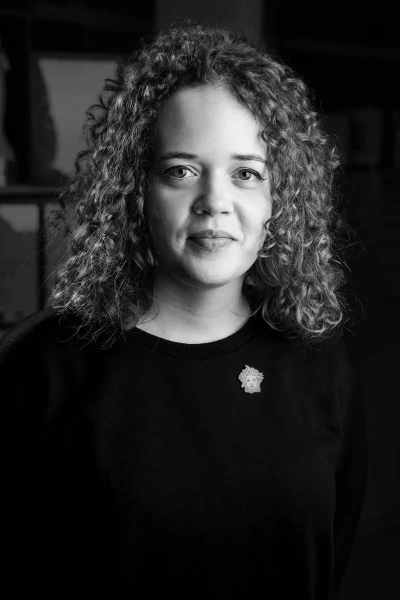 Black and white portrait of a woman with curly hair wearing a dark sweater with a decorative brooch.