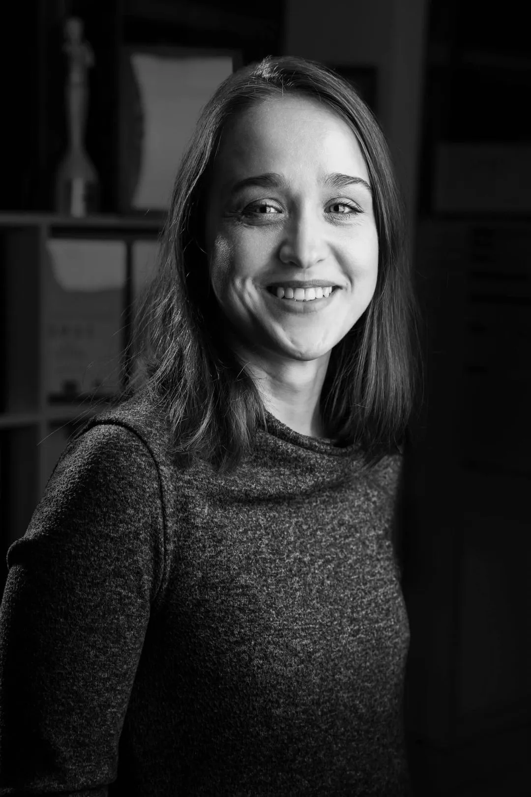 Black and white portrait of a smiling woman with shoulder-length hair wearing a textured sweater.