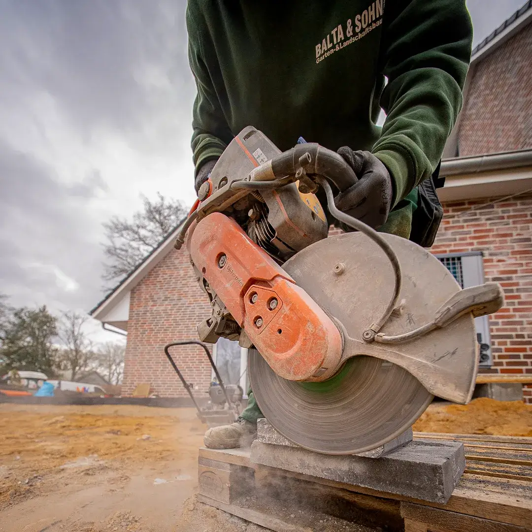 Arbeiter in grüner Jacke schneidet Pflasterstein mit einer großen elektrischen Steinsäge auf einer Baustelle.
