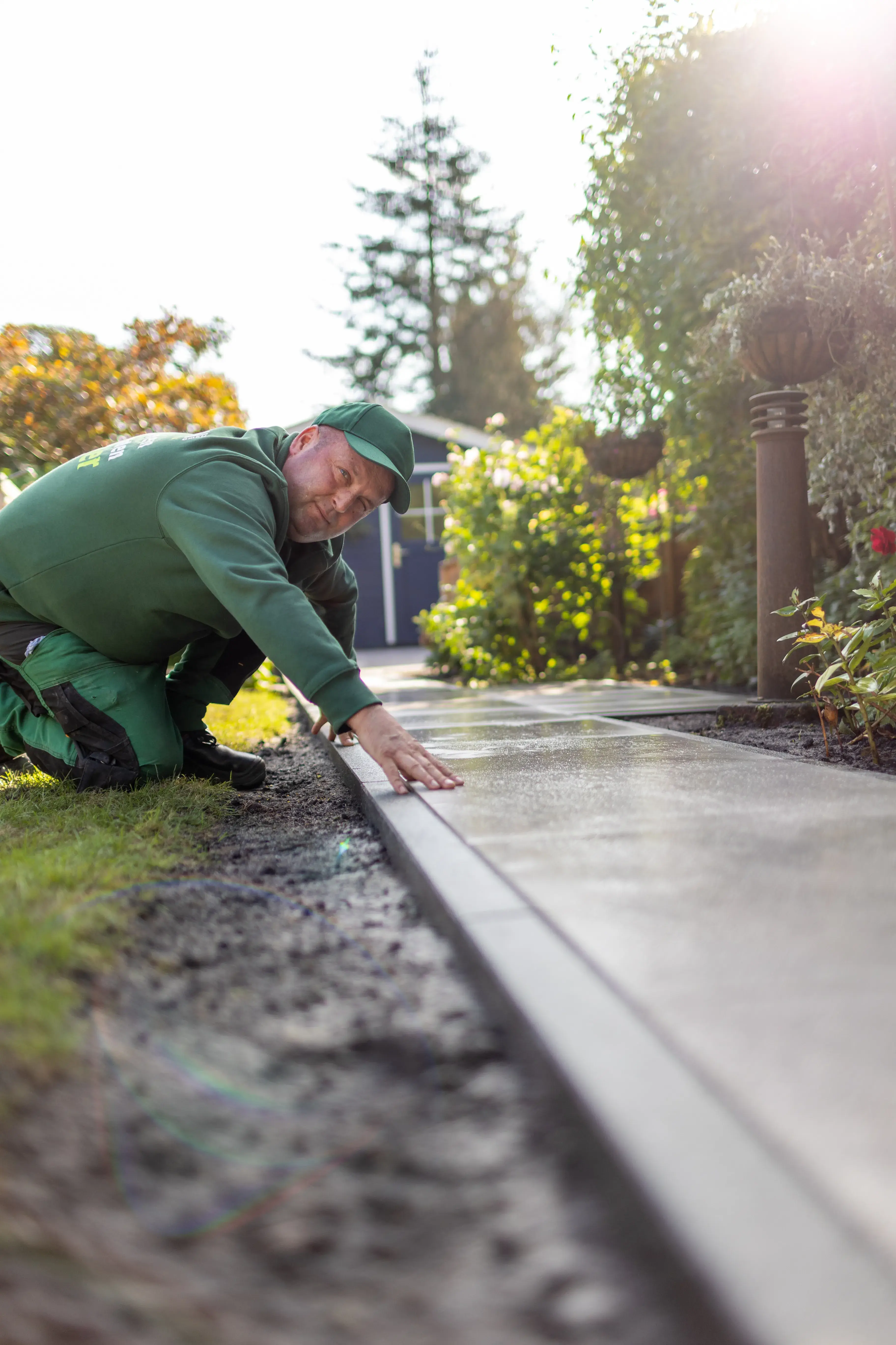 Gärtner überprüft Pflastersteine entlang eines Gartenwegs bei Sonnenschein.
