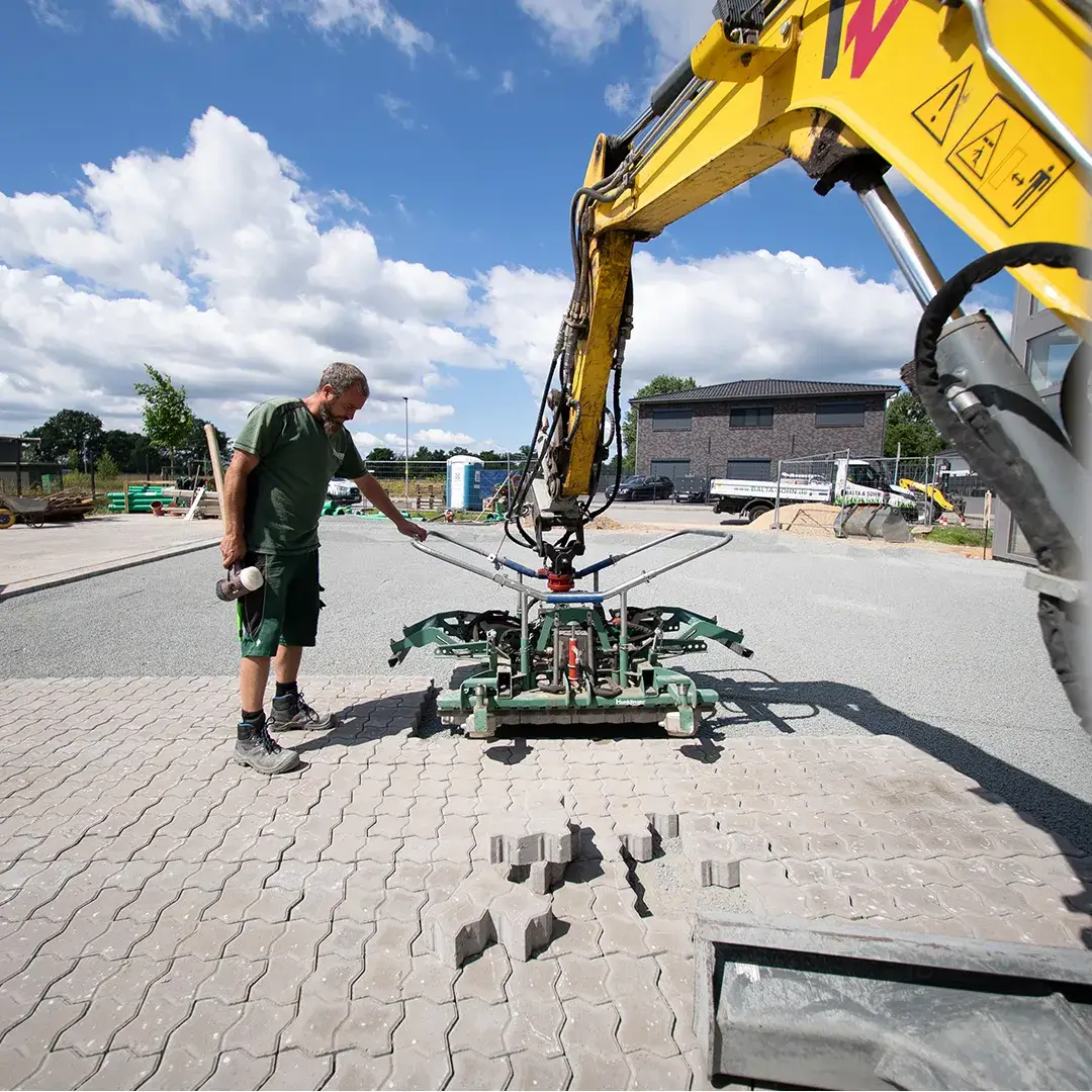 Mann bedient eine Maschine, die Pflastersteine auf einer Baustelle verlegt.