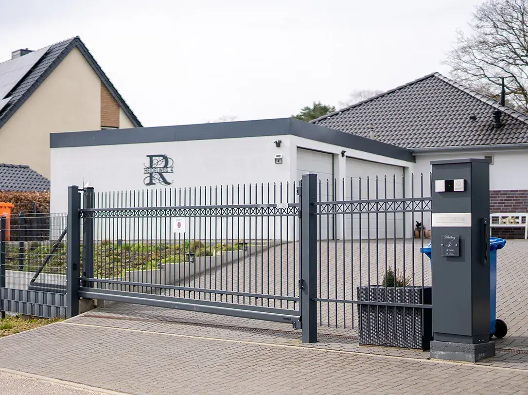 Modernes graues Metalltor vor Einfahrt zu einem weißen Haus mit Garage.