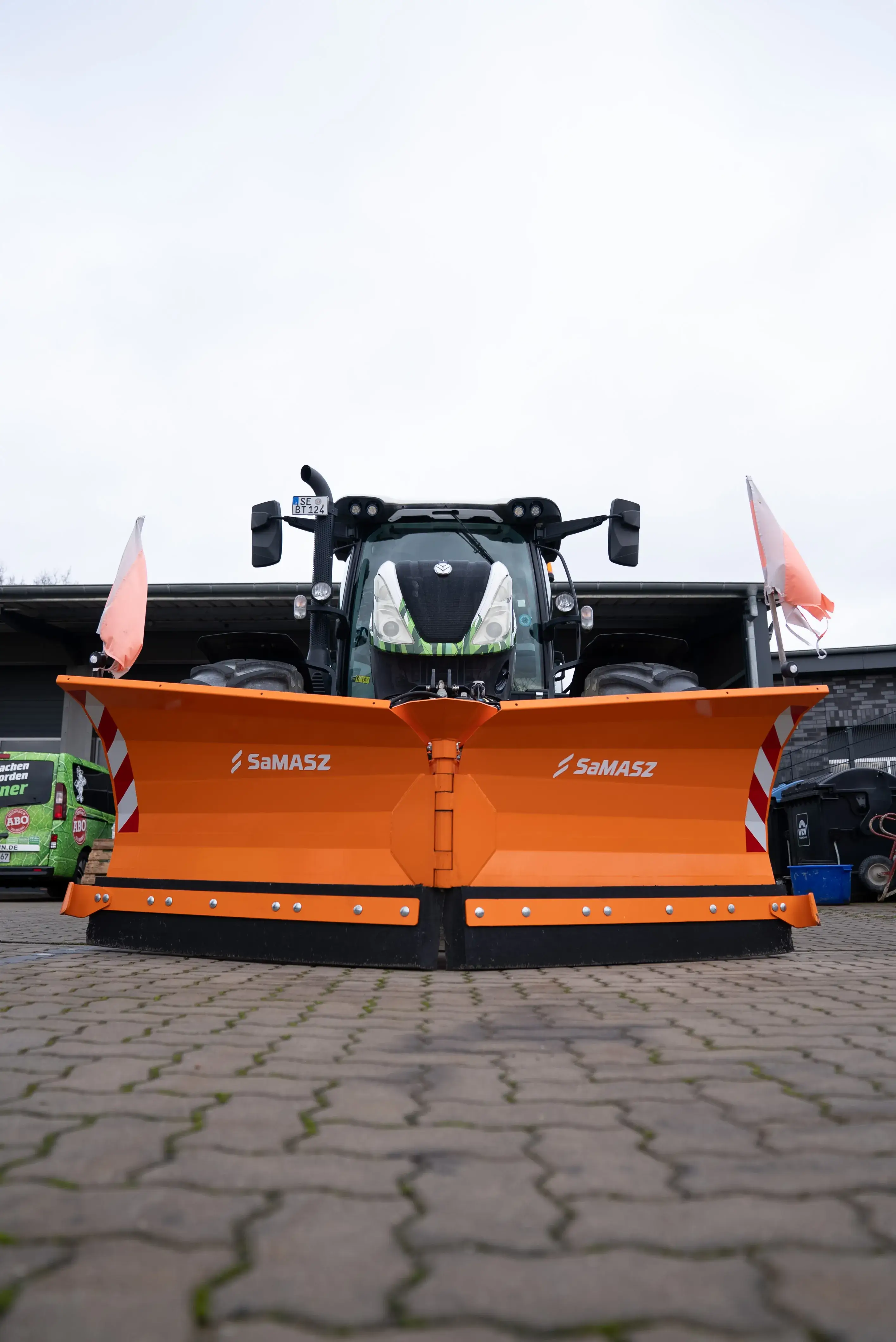 Oranger Schneepflug mit dem Aufdruck SaMASZ an der Vorderseite eines Traktors geparkt auf gepflastertem Boden.
