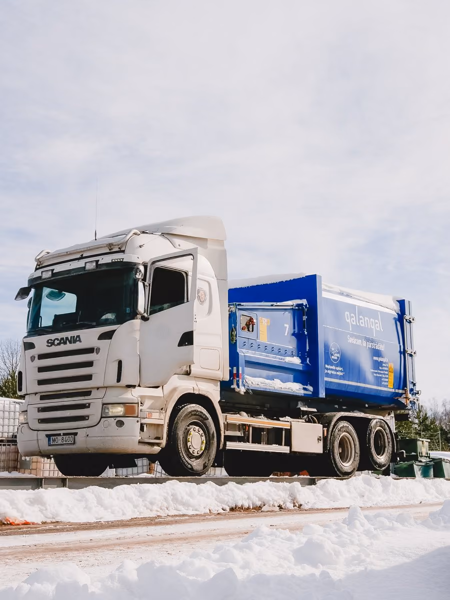 White Scania truck with a blue cargo container on a snowy road under a cloudy sky.