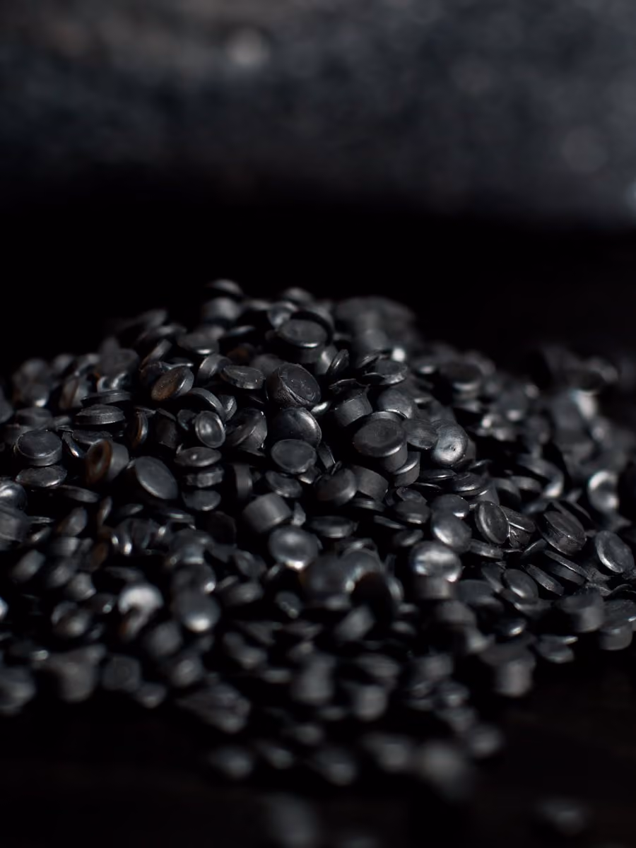 Close-up of a pile of small black plastic pellets on a dark surface.