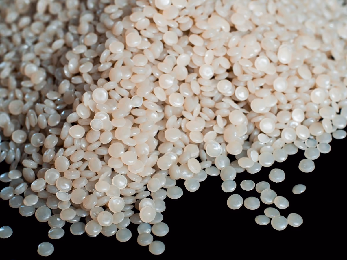 Close-up of numerous small, round, translucent white plastic pellets on a black surface.