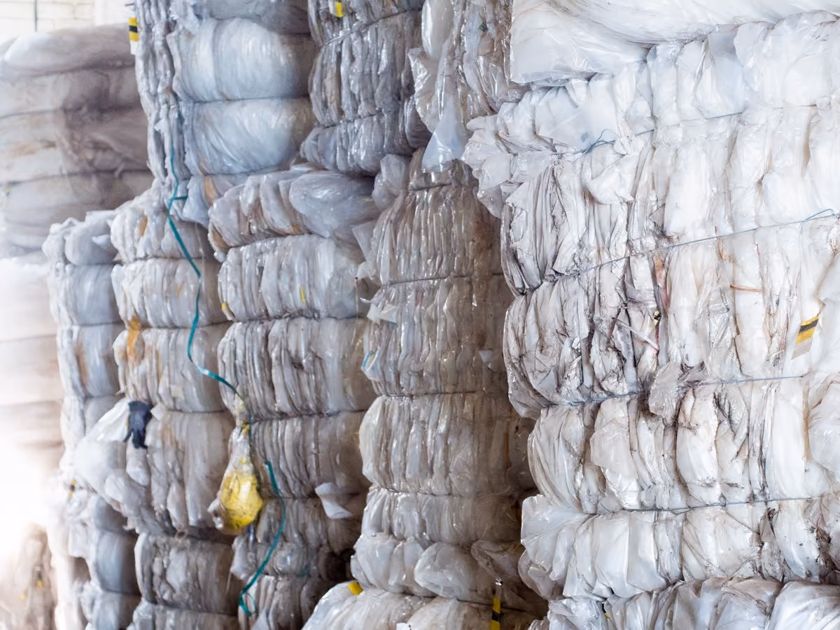 Stacks of compressed, white plastic bales tied with wires, likely in a recycling facility.