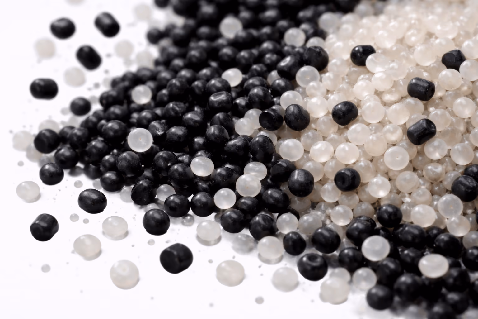 Close-up of scattered black and translucent small plastic pellets on a white surface.