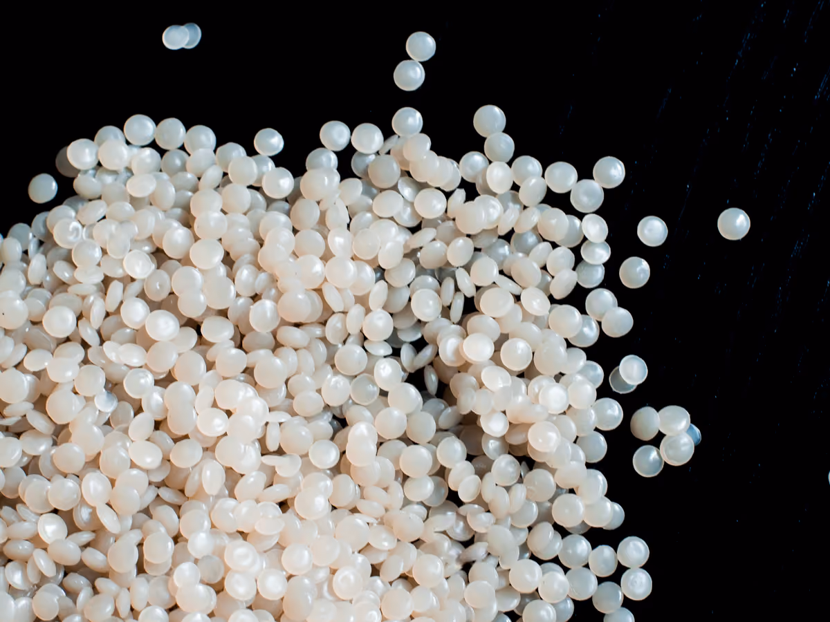 Close-up of small round translucent white plastic pellets scattered on a black surface.