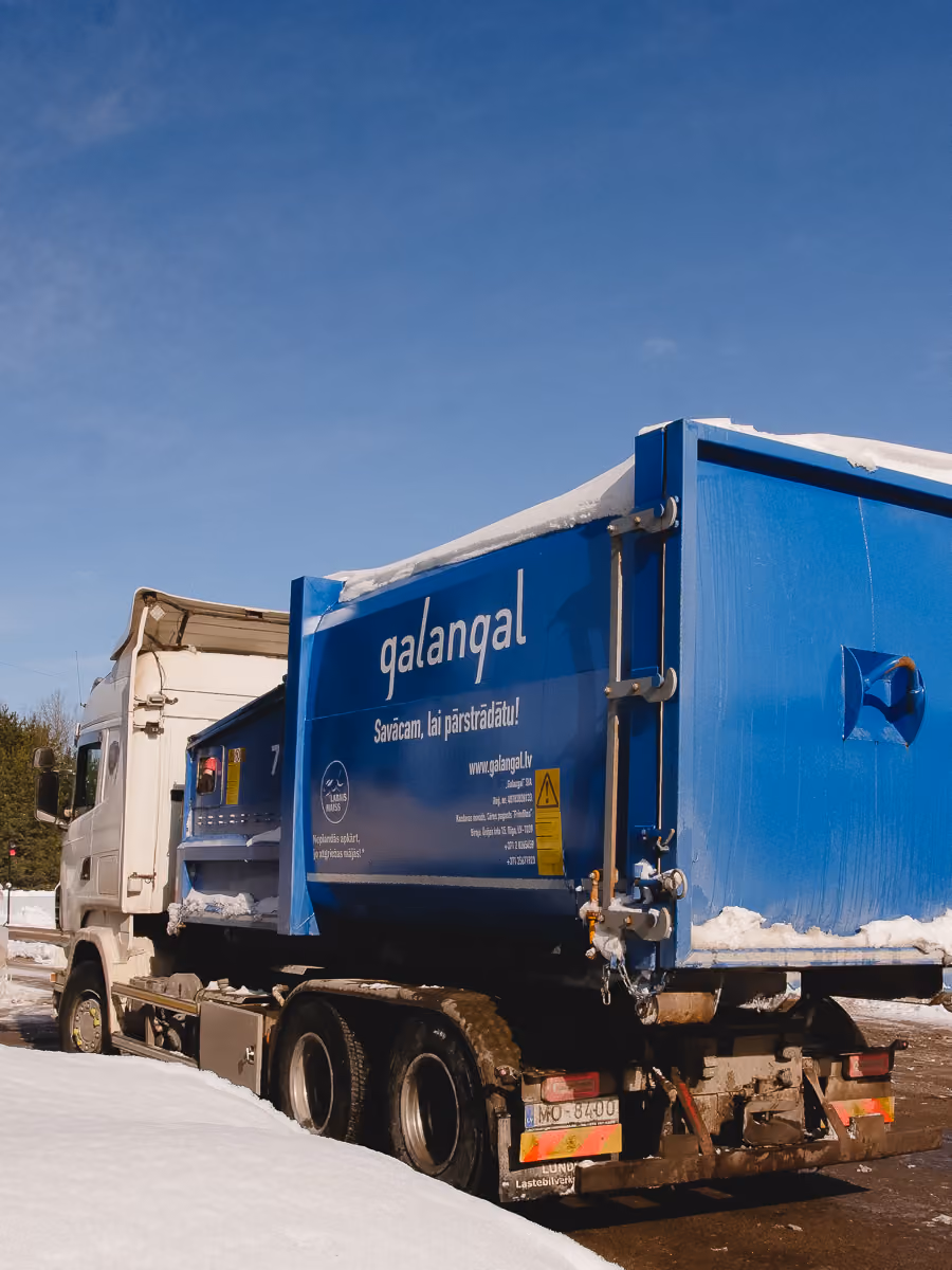 Blue dump truck with 'qalanqal' logo parked on snowy ground under clear blue sky.