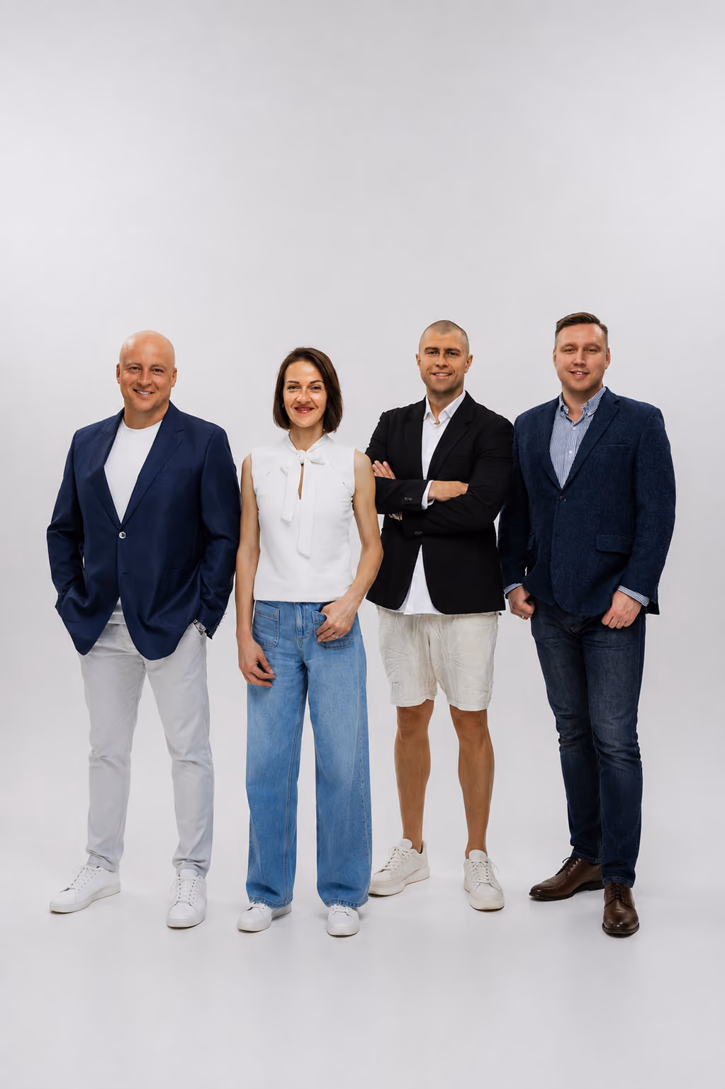 Four adults standing in a row against a white background, dressed in smart casual clothing.