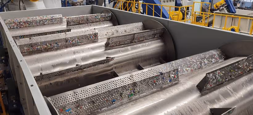 Industrial machine with rotating metal drums sorting small plastic waste pieces.