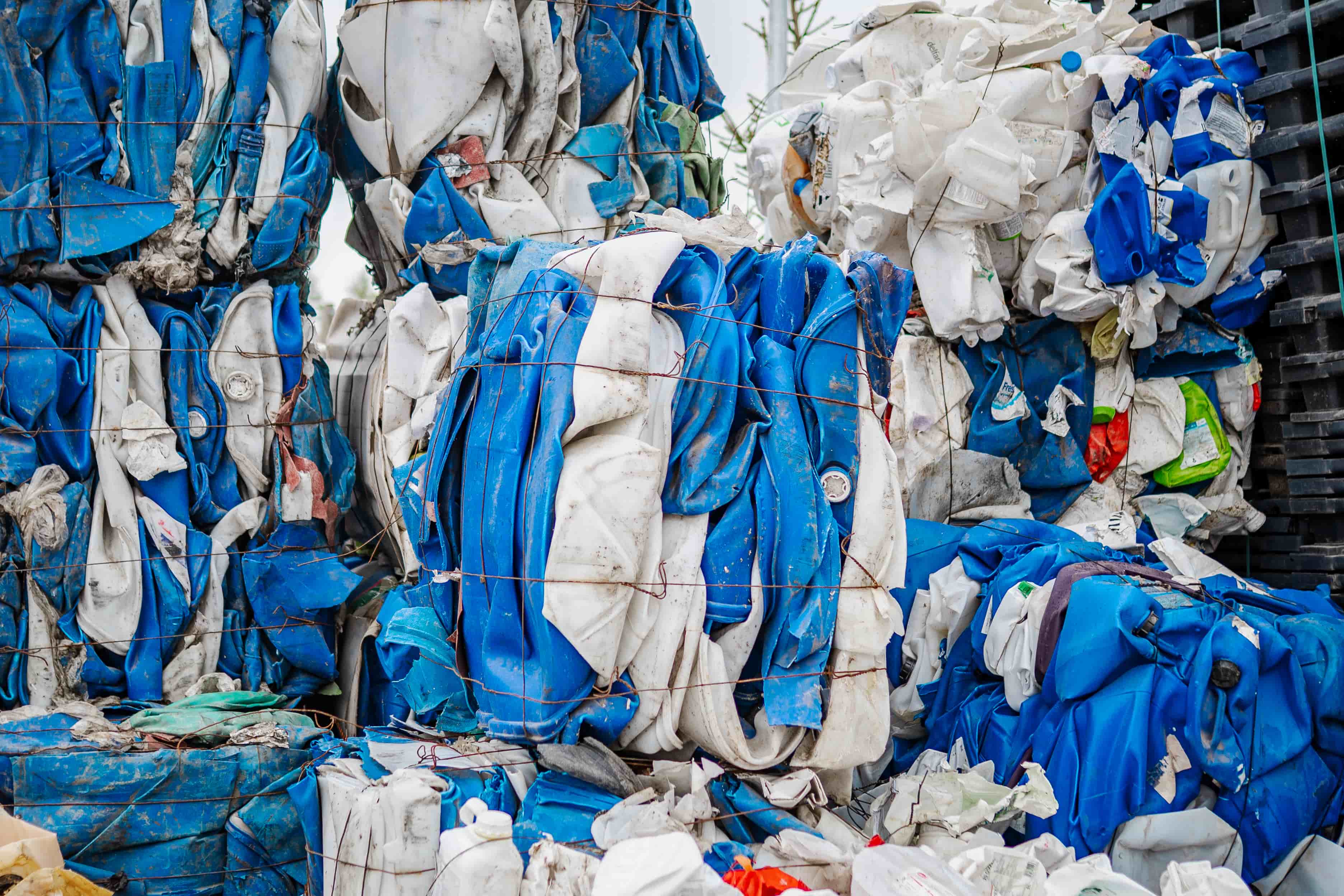 Baled and compressed blue and white plastic waste tightly bound with wire in a recycling facility.