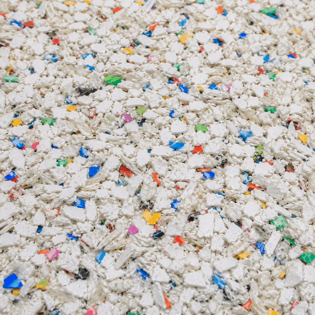 Close-up of crushed white plastic pieces with small colorful fragments mixed in.