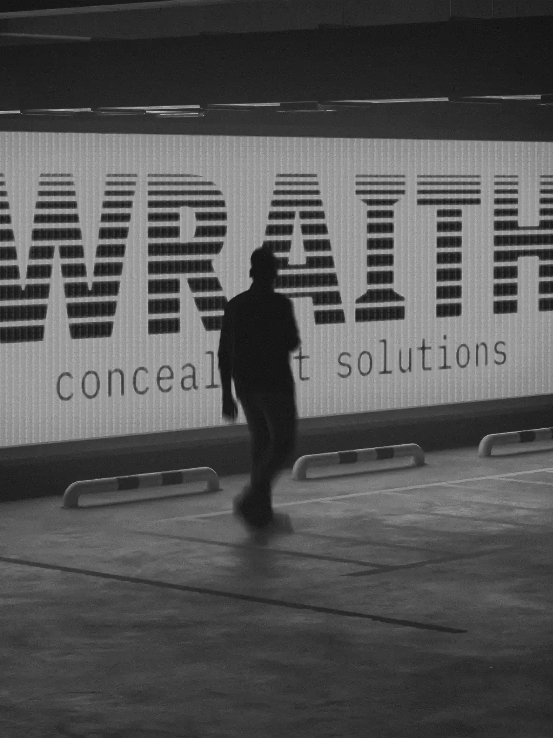 Silhouette of a person walking in front of a large illuminated sign reading 'Wraith concealment solutions' in a parking garage.