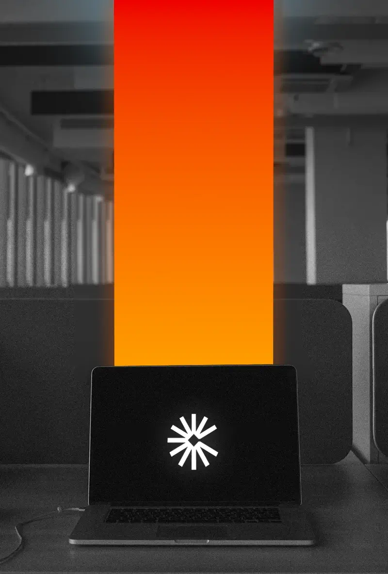 Laptop with loading symbol on screen displaying a vertical gradient beam from orange to red, set in an office environment.