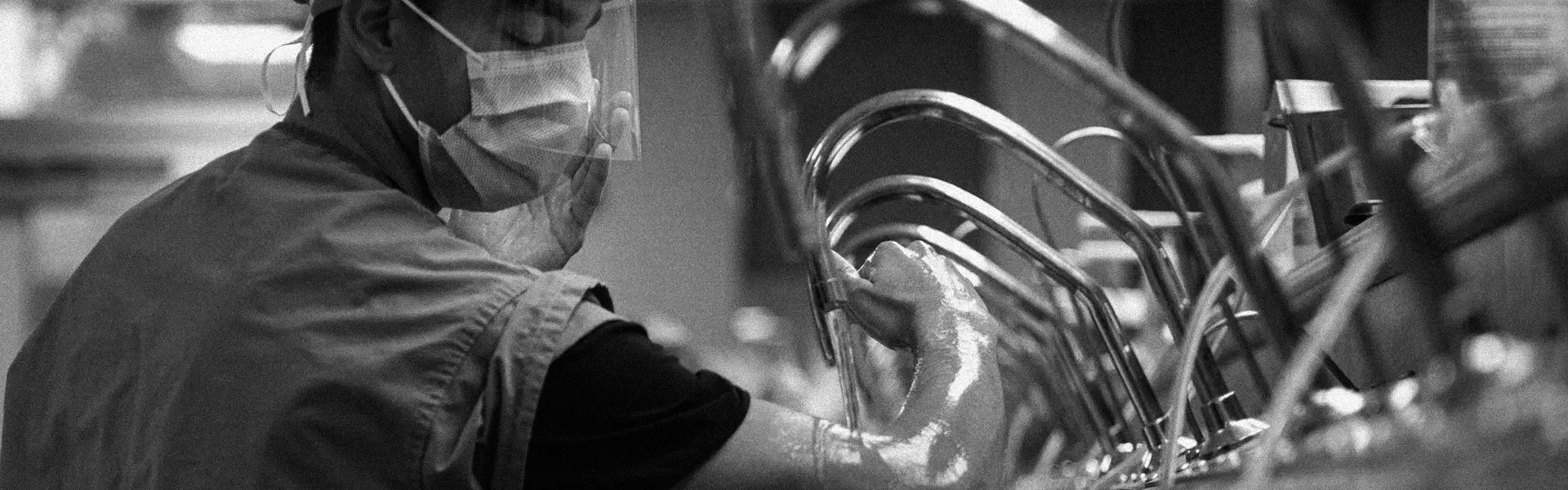 Healthcare worker wearing mask and face shield washing hands under hospital sinks.