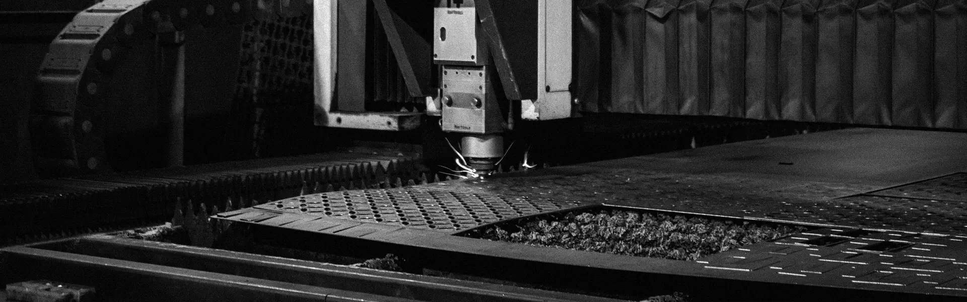 Close-up of an industrial CNC machine with sparks cutting a patterned metal sheet.