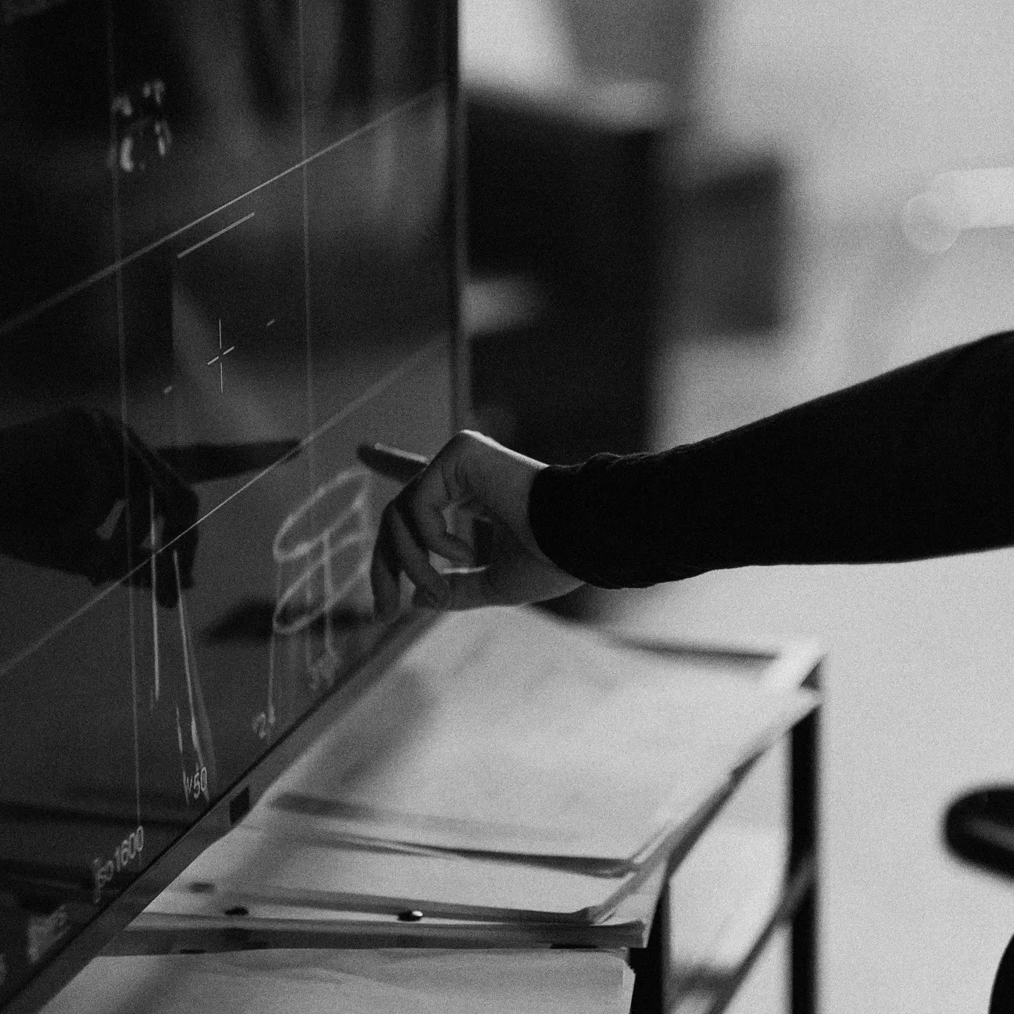 Person writing on a transparent board with charts and notes visible.