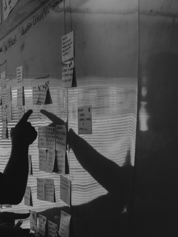 Silhouetted hands pointing at sticky notes on a wall with shadows cast behind them.
