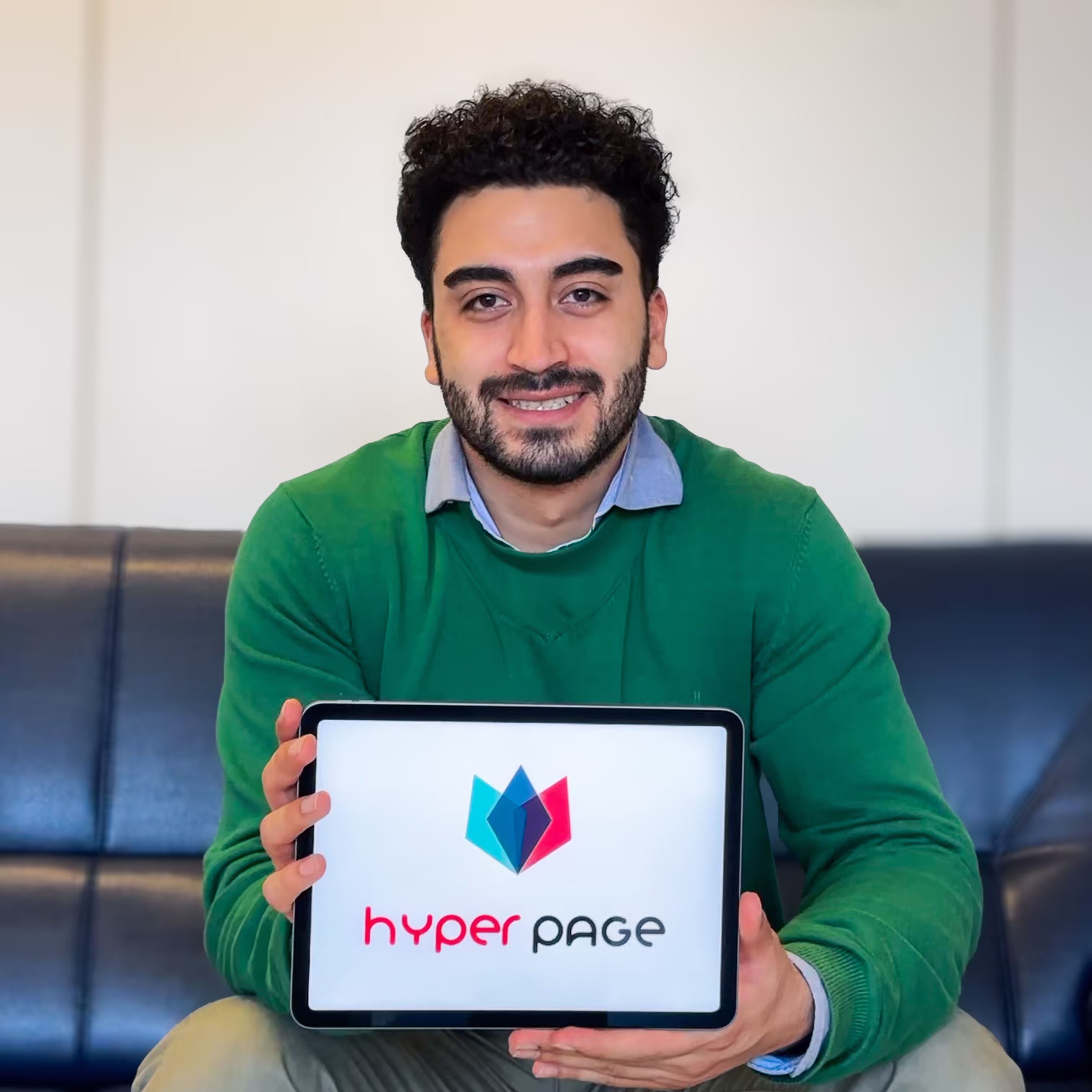 Mann mit grünem Pullover hält ein Tablet mit dem Hyper Page Logo.