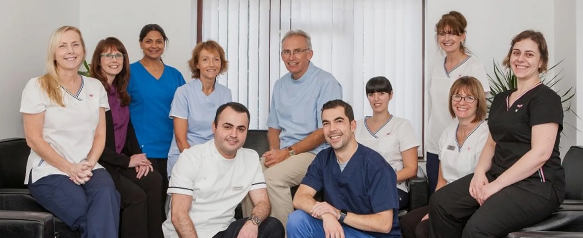 Group portrait of eleven medical professionals in scrubs and uniforms smiling indoors.