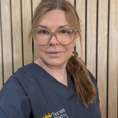 Woman with light brown hair in a ponytail wearing large clear glasses and a navy scrubs top with a dental clinic logo.