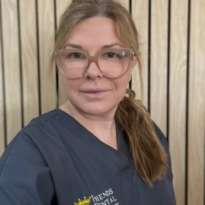 Woman with light brown hair in a ponytail wearing large clear glasses and a navy scrubs top with a dental clinic logo.
