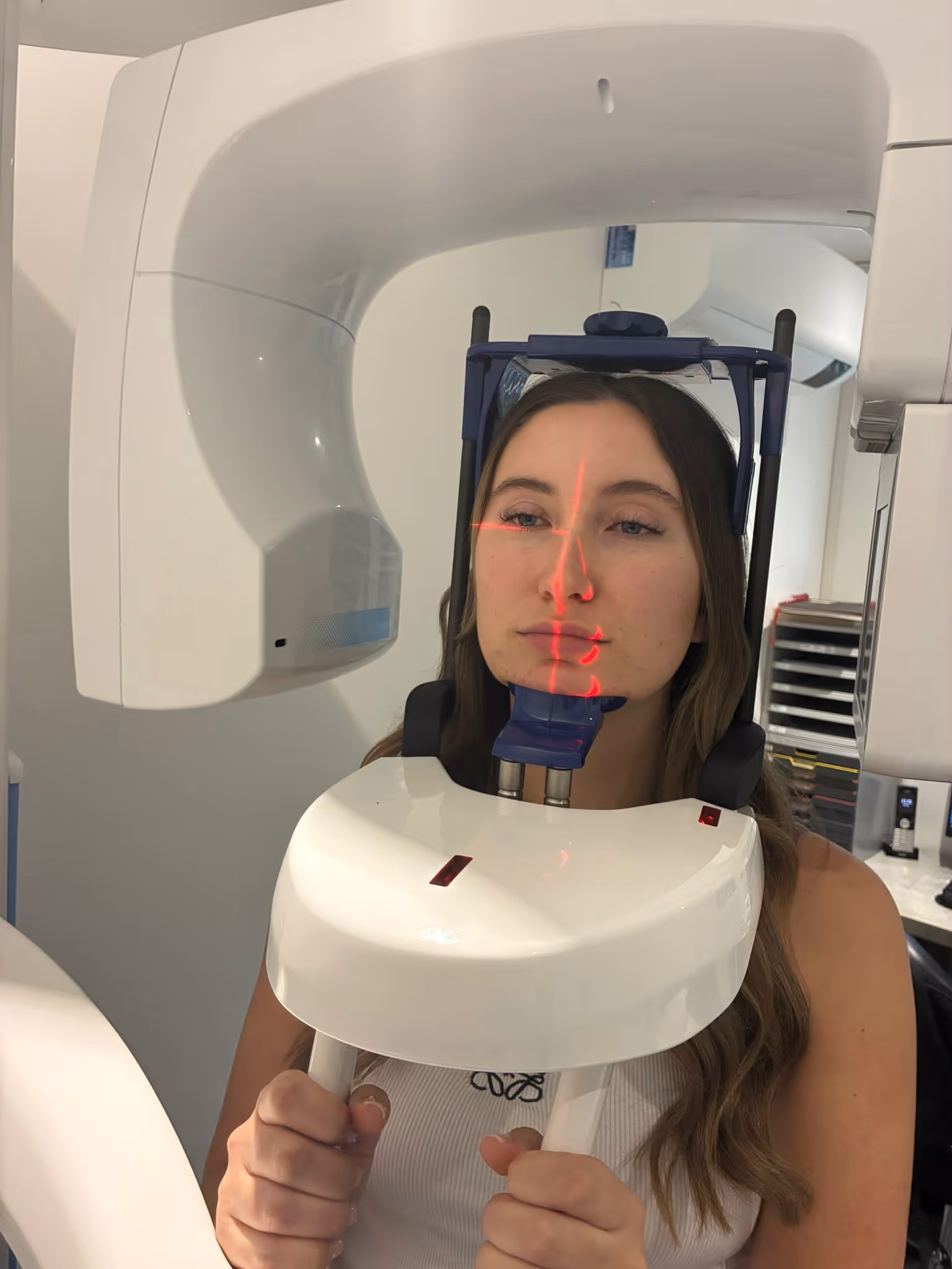Woman undergoing a dental 3D X-ray scan with red laser alignment on her face.