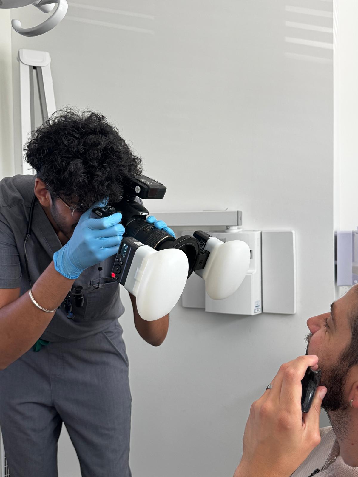 Photographer wearing blue gloves taking a close-up photo of a man holding a black shaving tool to his beard.