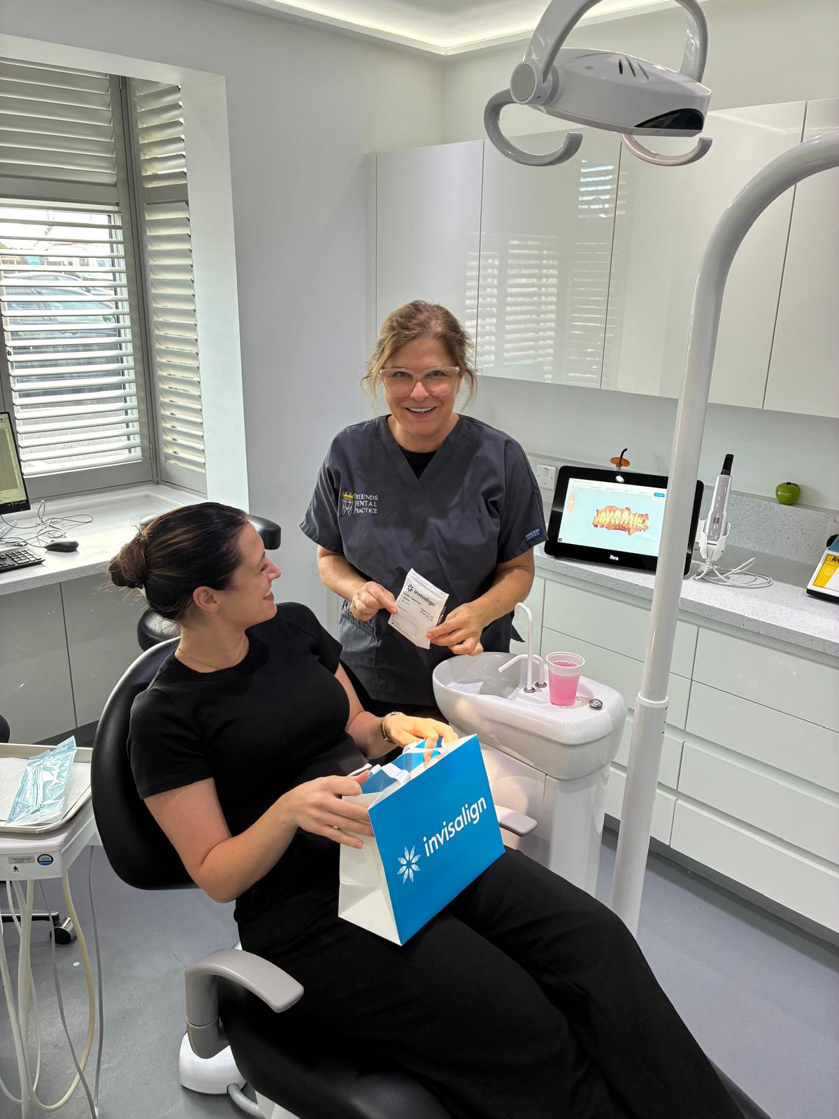 Smiling dental professional explaining Invisalign treatment to a seated patient holding an Invisalign bag in a modern dental clinic.