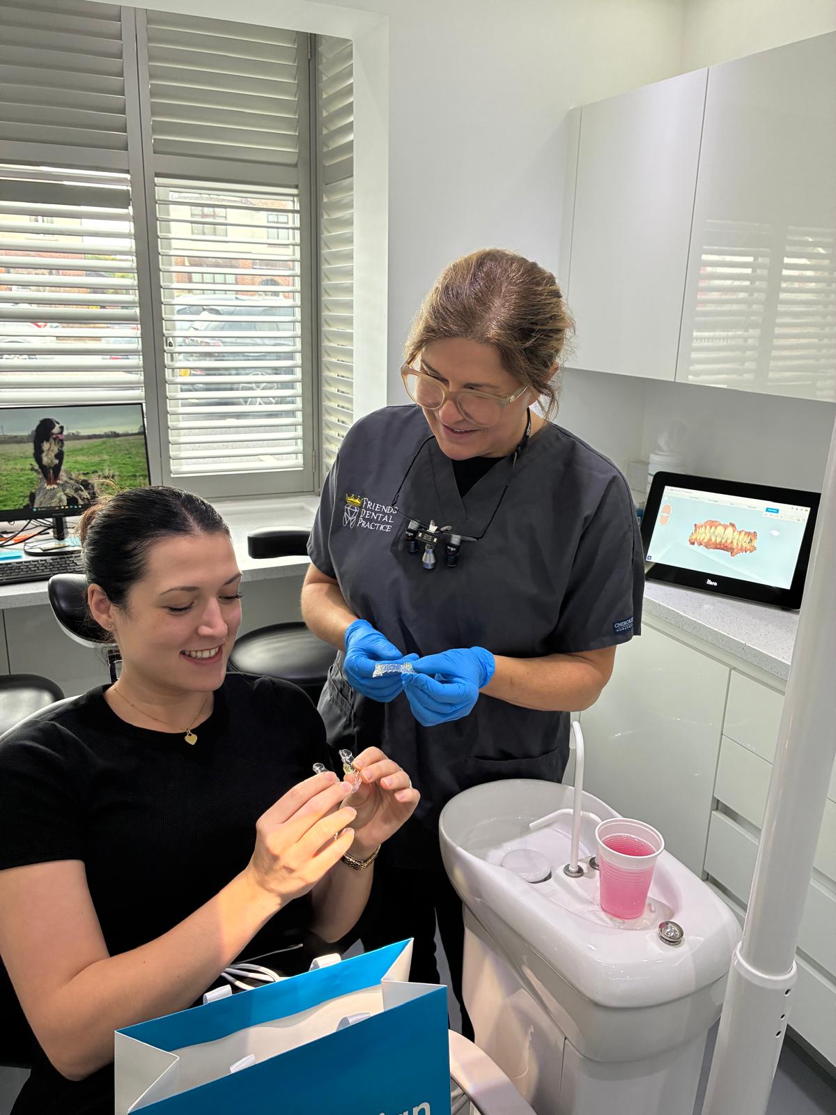 Dentist in blue gloves showing clear dental aligners to a smiling female patient in a dental office.