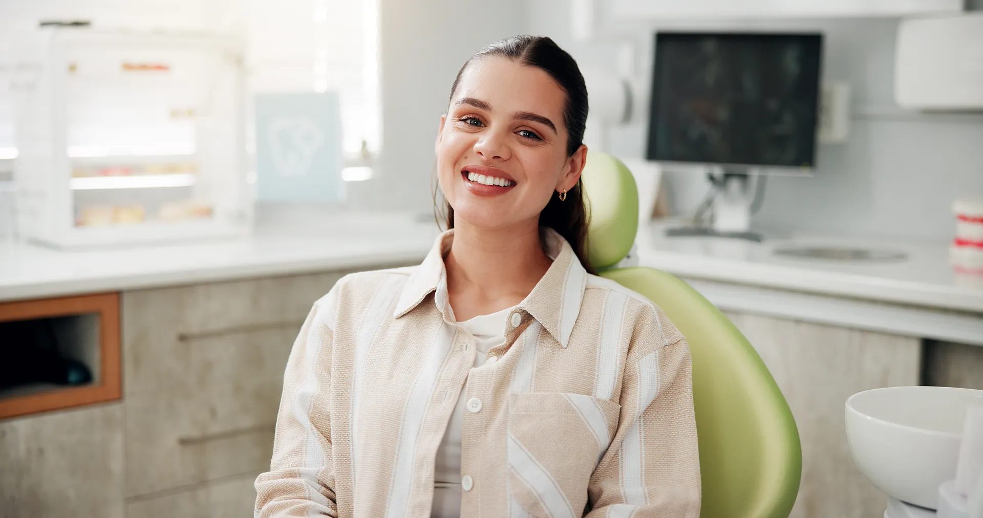 Smiling woman sitting in a green dental chair in a bright dental office.