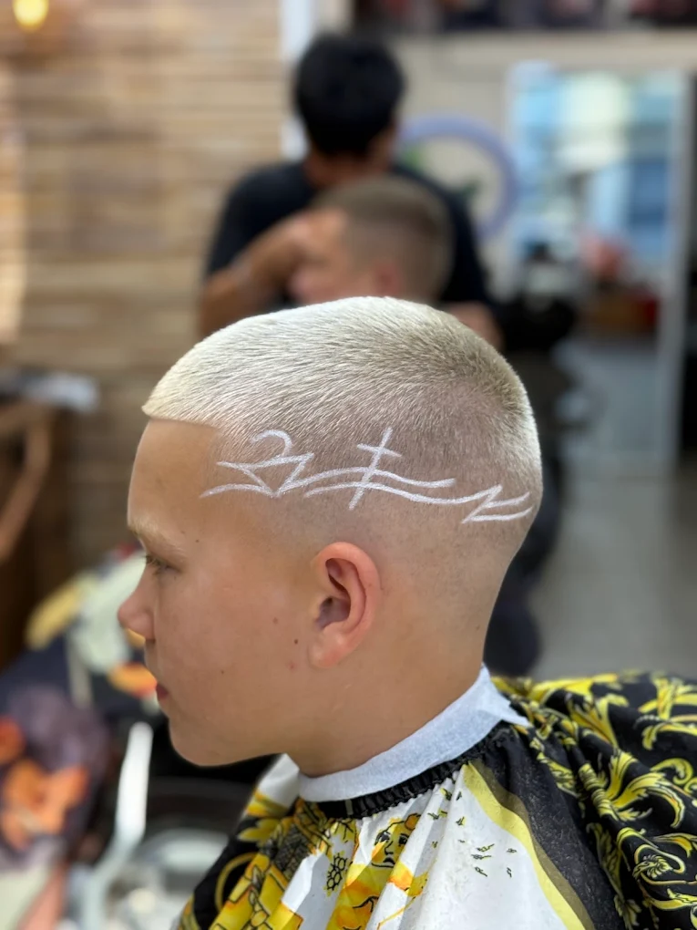Side profile of a person with platinum blonde buzz cut featuring a white abstract line design shaved into the hair on the side.