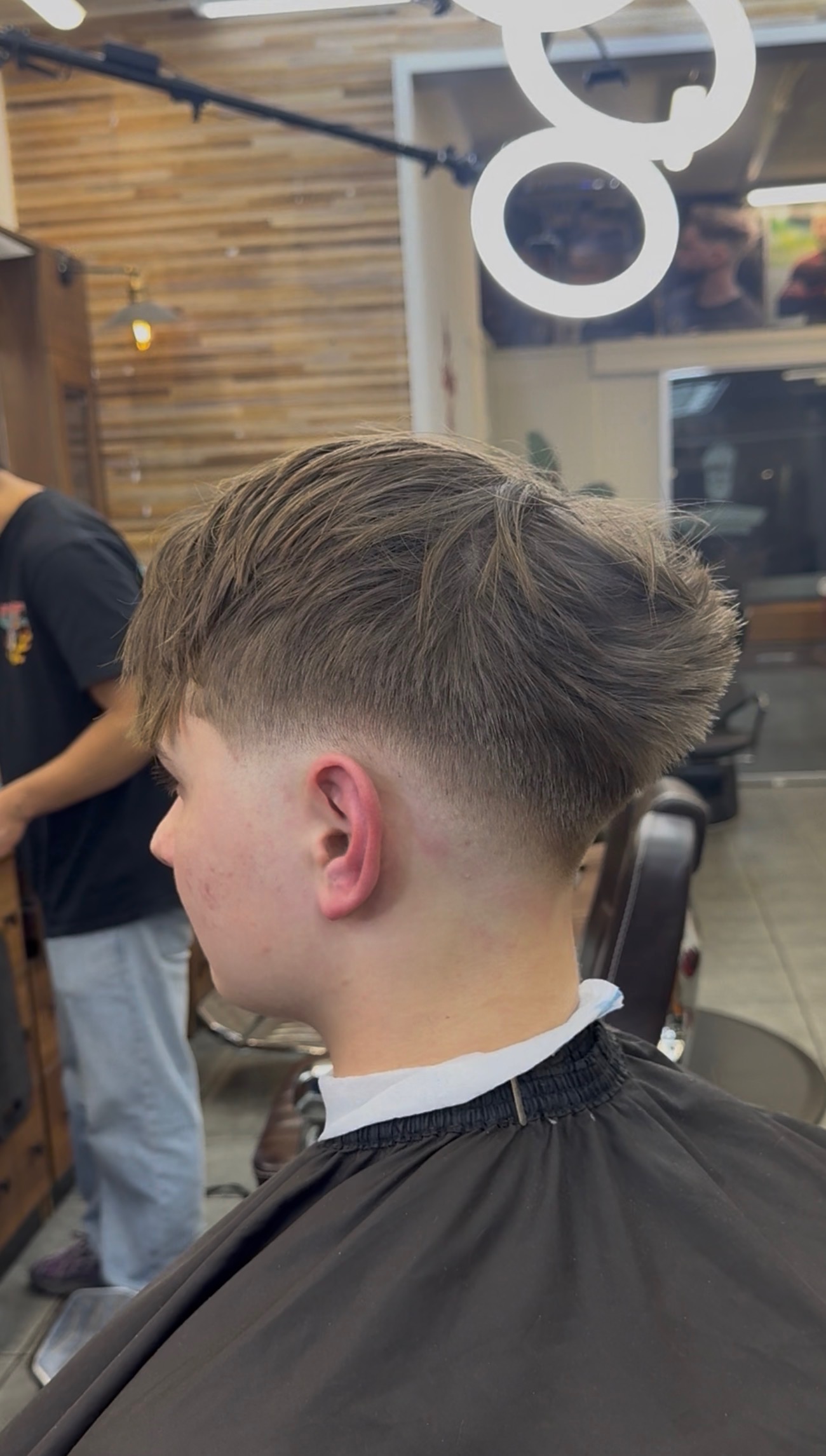 Side view of a young man with a fresh fade haircut in a barbershop, wearing a black barber cape.