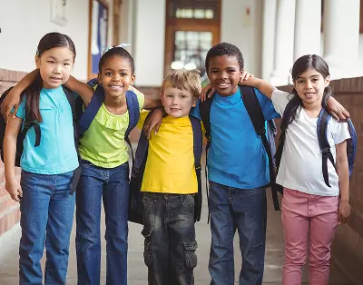 Five diverse students with backpacks smiling together outside school