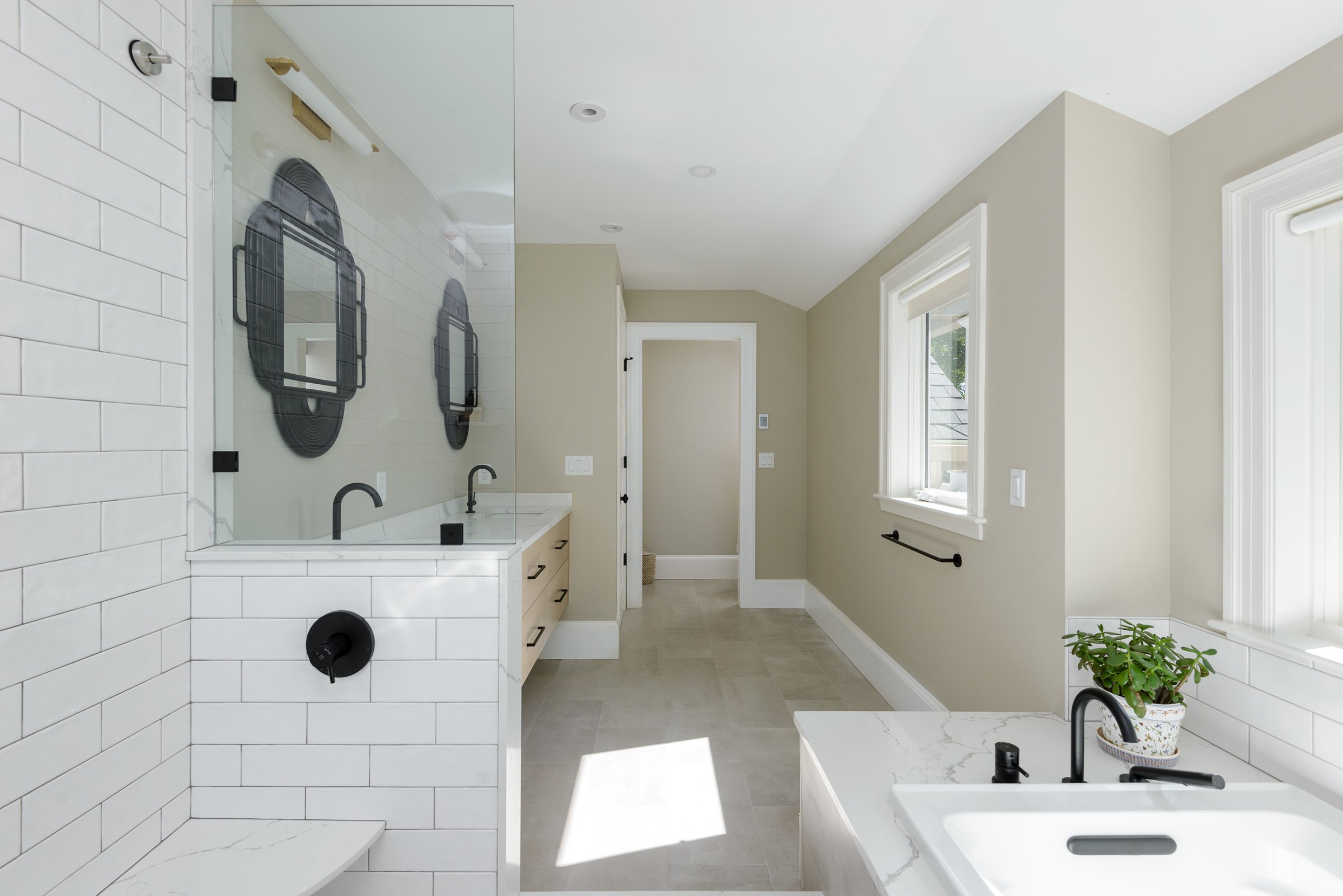 Undermount tub under twin windows with white subway tile and matte black plumbing in Hingham primary bathroom.