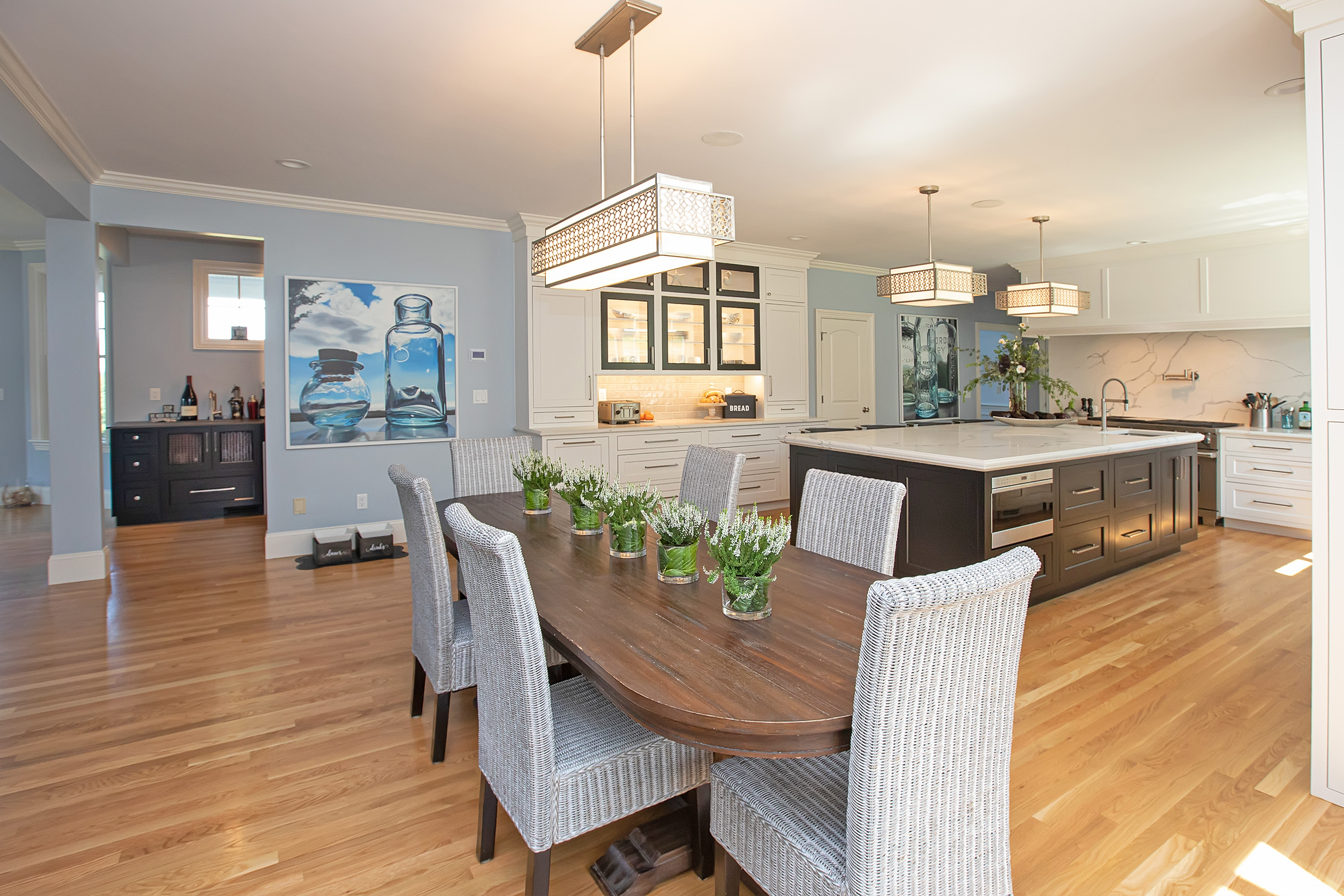 A Hingham first floor remodel by Transitions with a white beaded inset Mouser kitchen, custom hutch, built-in bar with wine fridge, and a refreshed fireplace mantel.