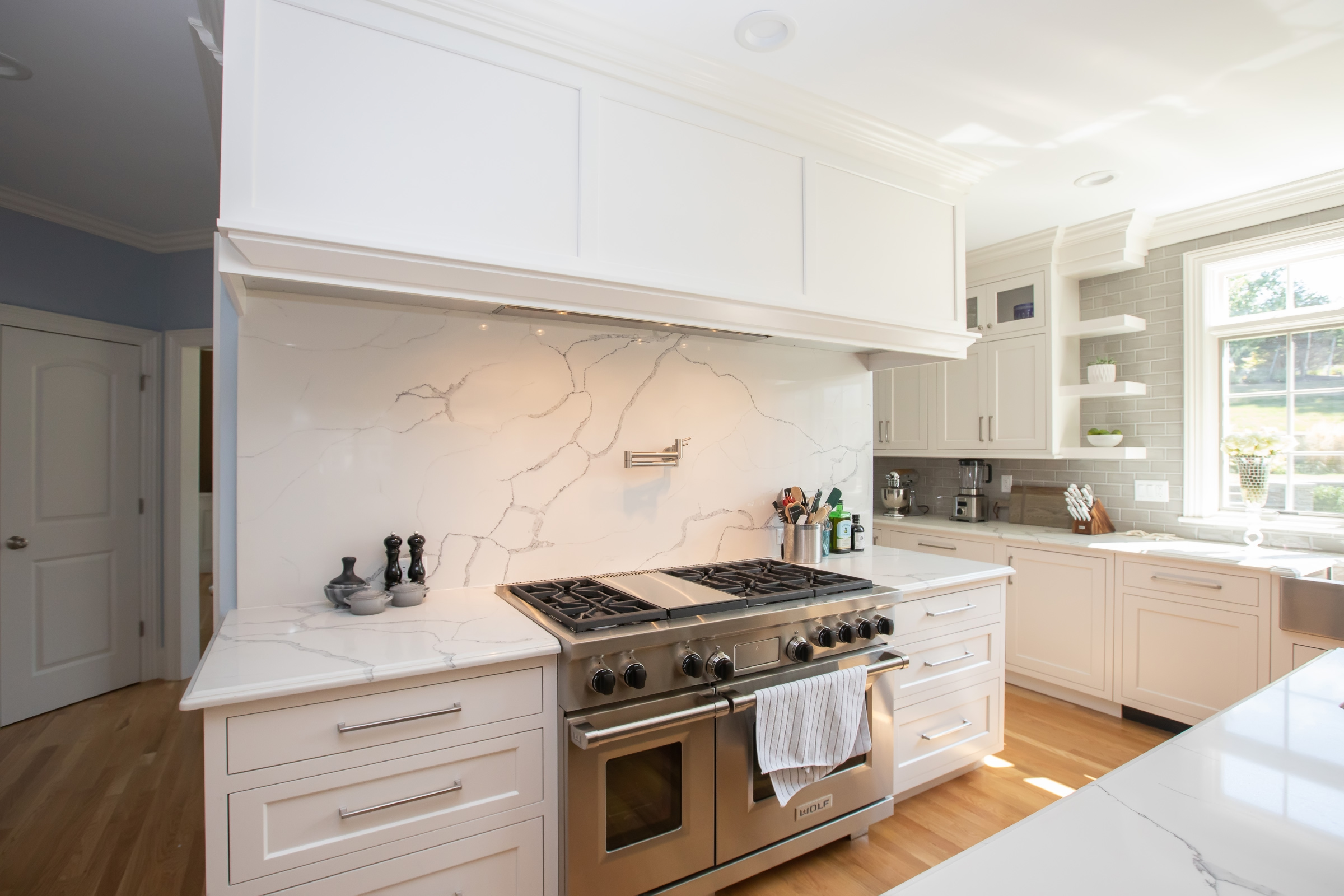 Cooking wall with stainless range, gray glass tile backsplash, and white Mouser cabinetry in Hingham