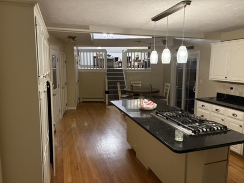 Original Hingham kitchen before remodel with cream cabinetry, dark granite counters, and the second floor staircase rising directly off the kitchen