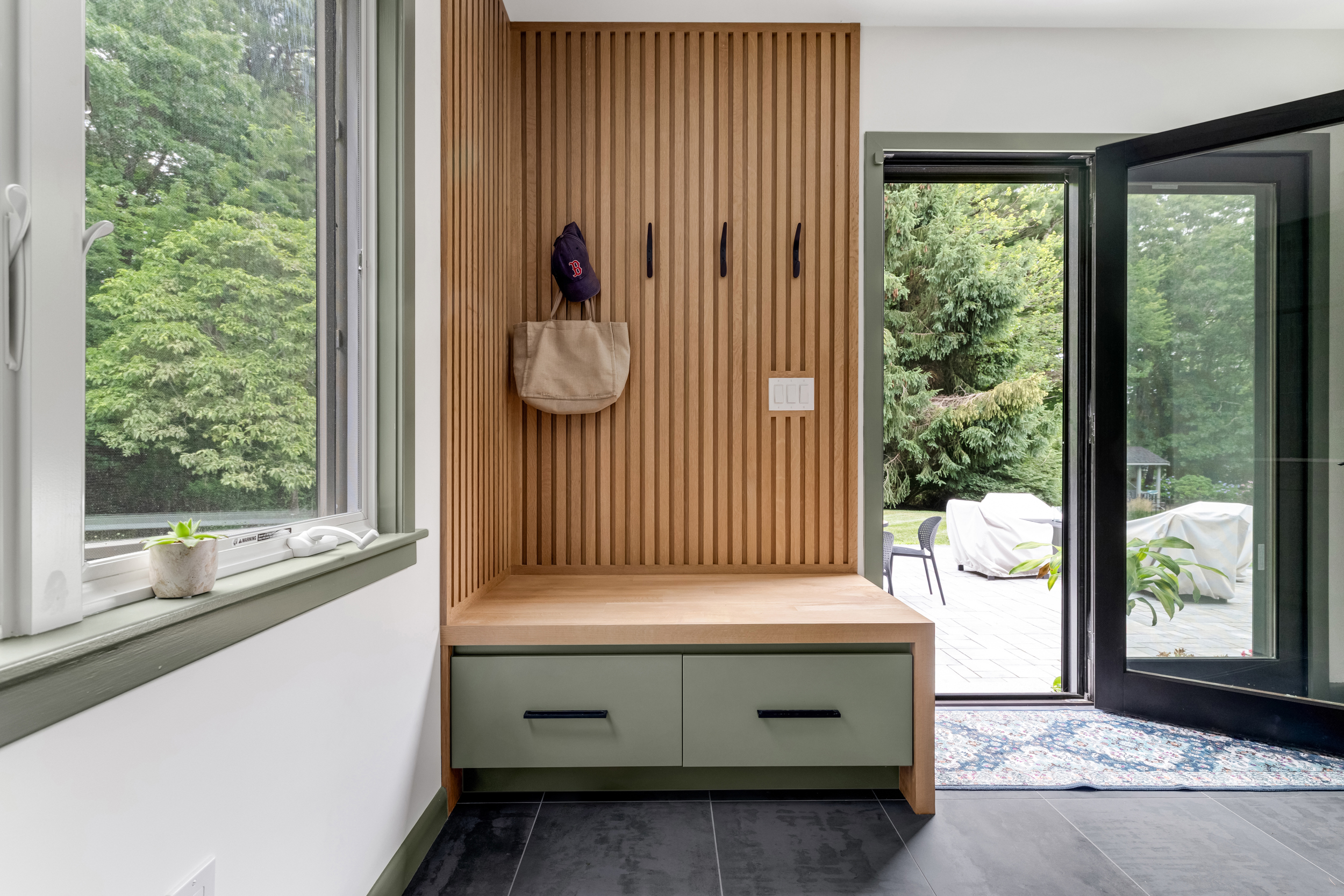  Built-in white oak mudroom bench with sage-green drawers and black hooks in a Marshfield addition