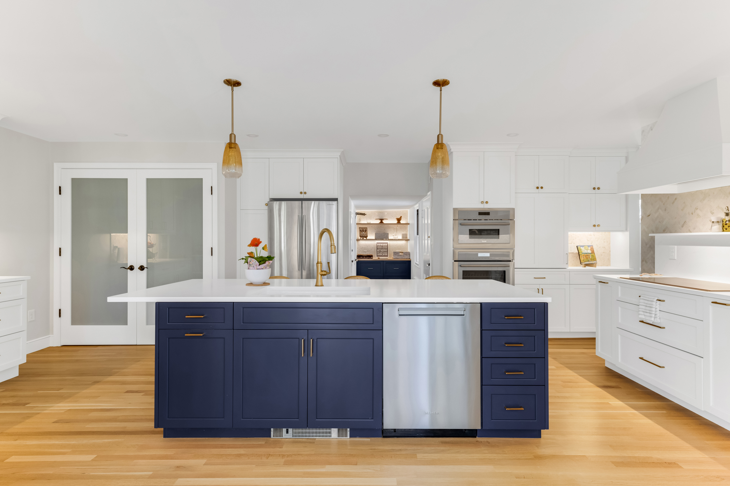 Milton kitchen with a navy shaker island, white perimeter cabinetry, brass hardware, and white oak flooring