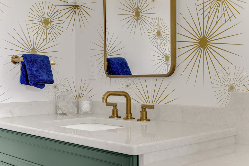 Brass widespread faucet on a white quartz vanity against gold starburst wallpaper in Hingham