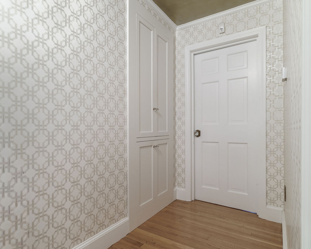 Recessed white linen cabinet with geometric wallpaper in the hall of a Hingham primary bath remodel